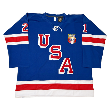 1960 USA Men's Hockey jersey blue USA in red with white outline diagonal left down to right. Red, white, red bands mid-sleeve and around waist. USA shield right chest. Royal Retros