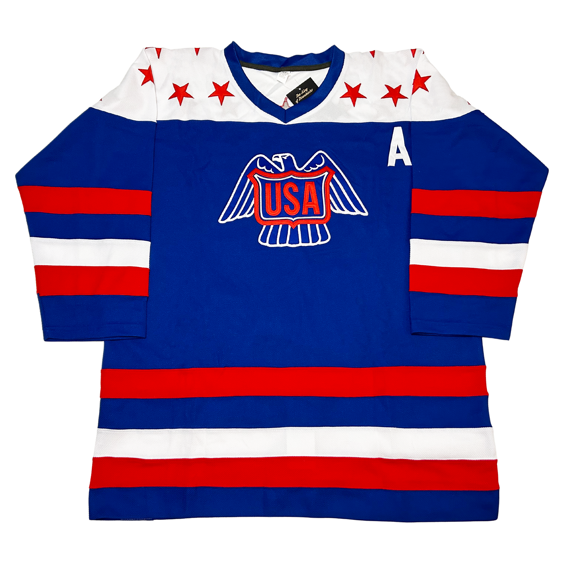 1976 USA Canada Cup Jersey. Blue. Red, blue, white, red bands on sleeves and waist. Eagle line drawing in white on chest with USA shield in red. Co-captain A on left chest. White shoulders with red stars. Blue trim on neck. Royal Retros