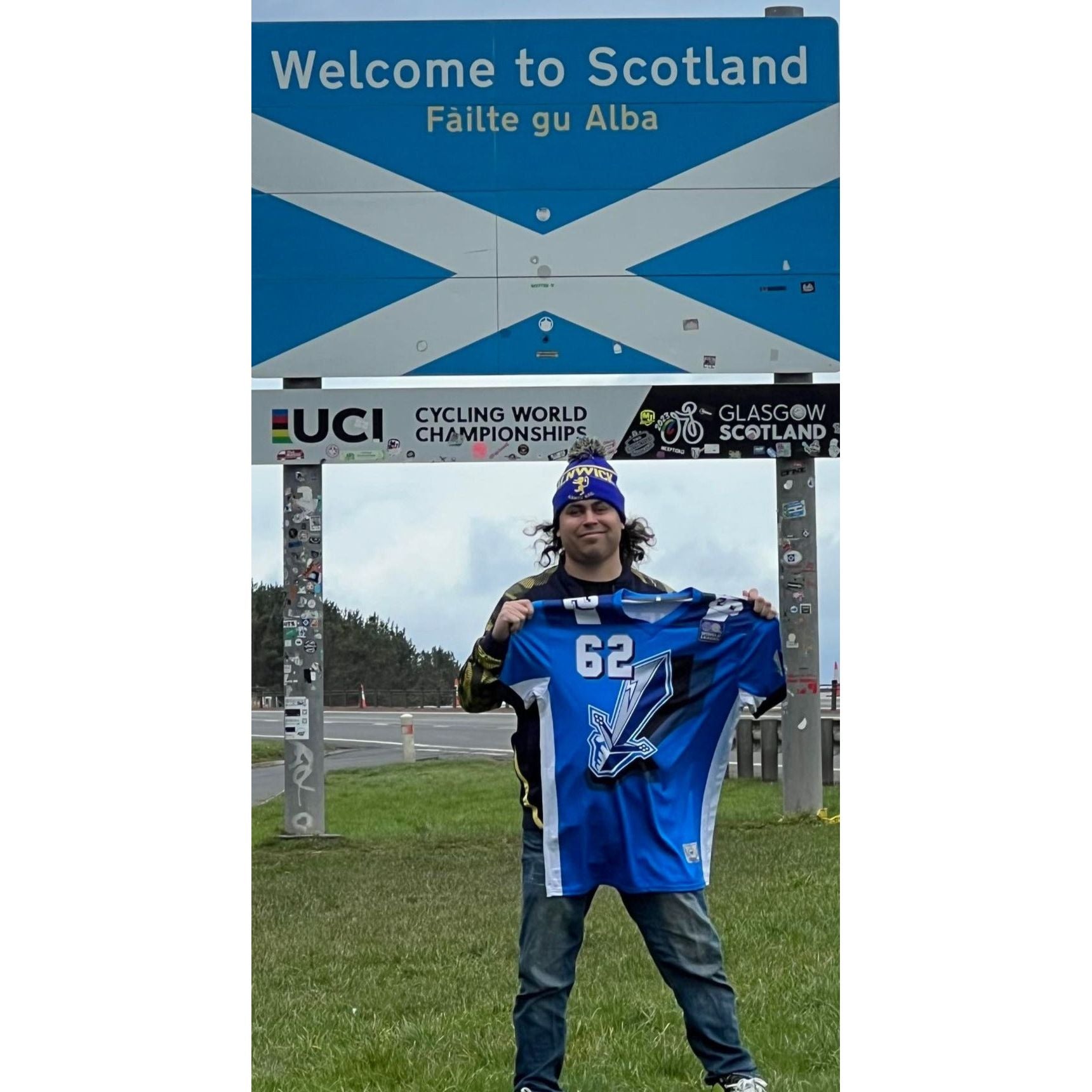 Fan wearing Scottish Claymores Graphic Jersey blue with silver #62 under Welcome to Scotland sign Royal Retros