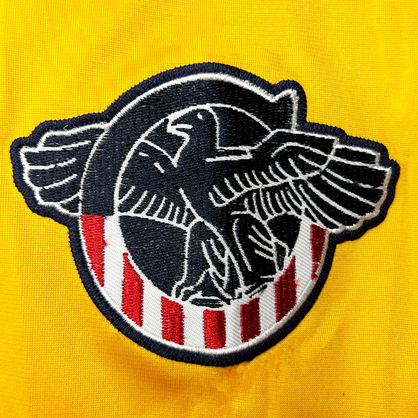 Cleveland Rams patch. C, top half navy blue with white trim. Red and white vertical stripes below. Stylized eagle with white detail resting inside C all on yellow jersey. Royal Retros