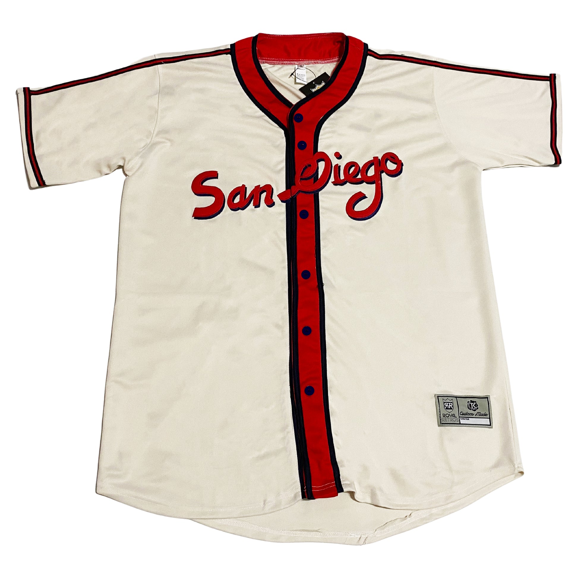 PCL Padres Home Button-up Jersey 1941. White. San Diego in cursive across chest, red with blue trim. Thick red band around neck and down front with blue trim. Red and blue trim around sleeve ends and across shoulders. Royal Retros