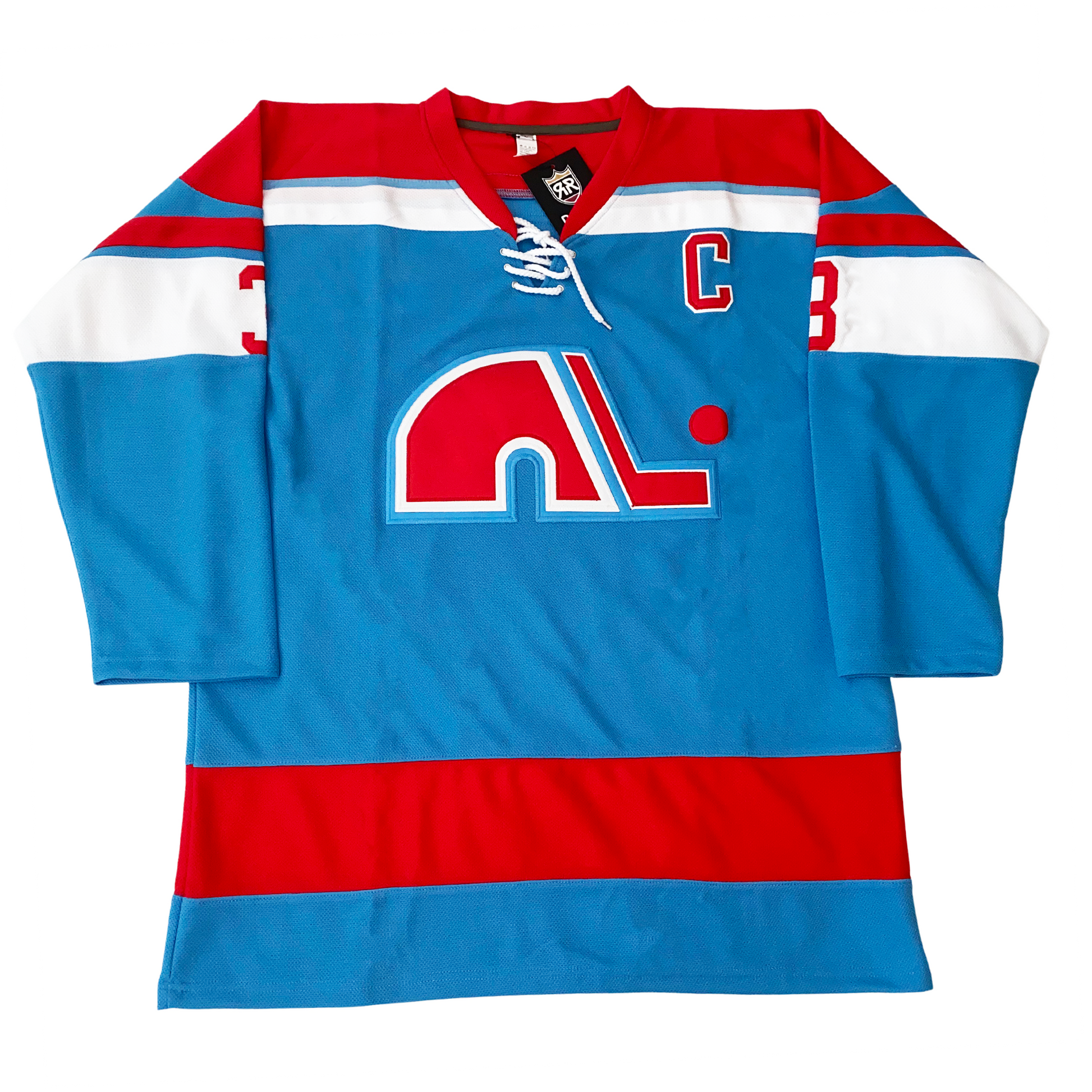 1972 WHA Nordiques Jersey. Blue. Red shoulders with white band around. Red, blue, and larger white bands on upper sleeve. Red band above waist. Red lowercase N logo with white trim. Red hockey stick to right of N with white trim,  red puck above blade. Captain C in red with white trim on upper left chest. Royal Retro