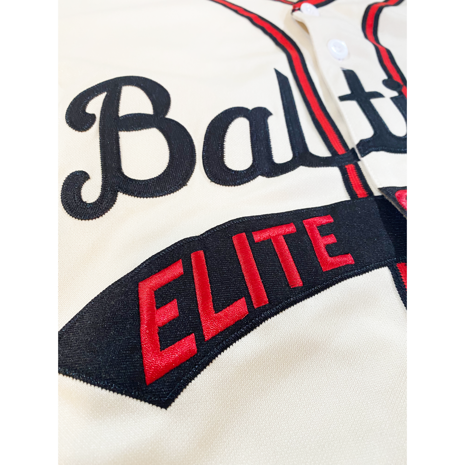 Close up of Baltimore Elite Giants jersey. White. Baltimore in black cursive across chest, Elite Giants in red inside text tail. Royal Retros