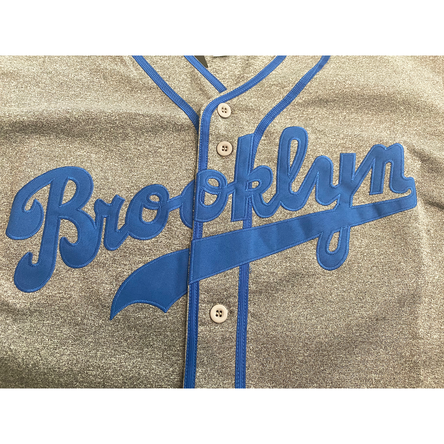 Brooklyn Dodgers pepper gray button-up baseball jersey close-up. Brooklyn in cursive in blue with text tail. Royal Retros