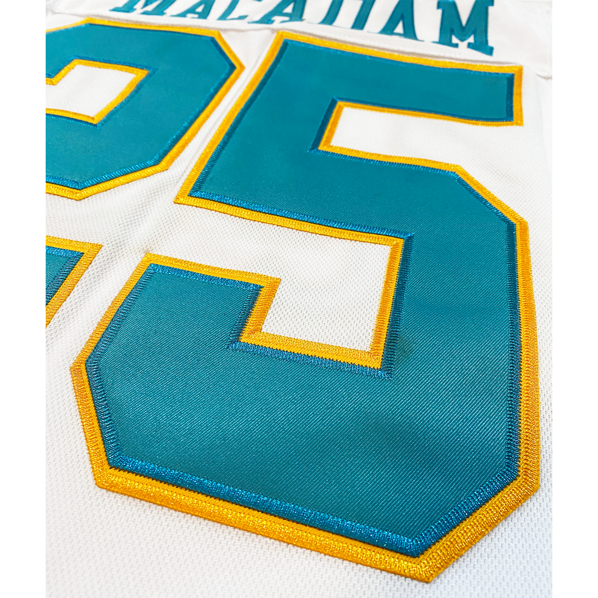 California Golden Seals Jersey white close-up of white jresey, #25 in teal with gold trim. Lettering above number in teal. Royal Retros