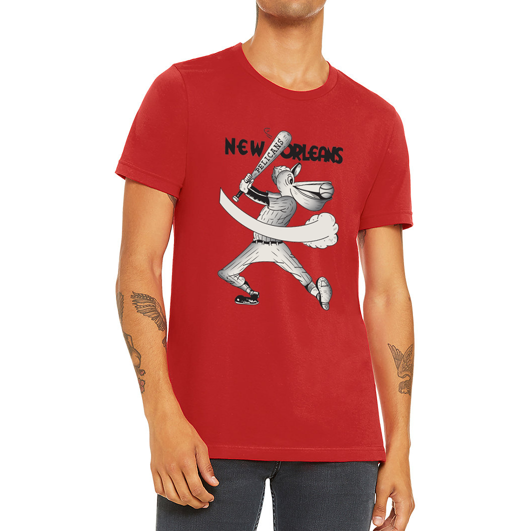 New Orleans Pelicans T-shirt. Red. New Orleans in black across top of shirt. Cartoon pelican, white with black detail swinging a bat. End of bat overlays "New Orleans" and has "Pelicans" wriiren on it. Royal Retros.